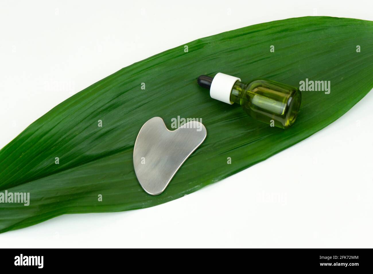 An unbranded green CBD cannabis oil with a Gua sha massaging scraping tool lie on a green leaf Stock Photo