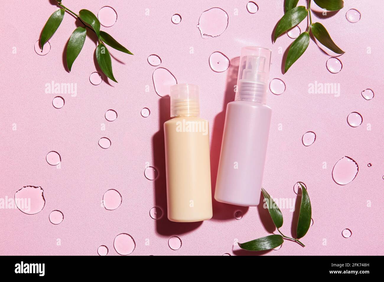 Bottles of cosmetic products and green leaves on color background with ...