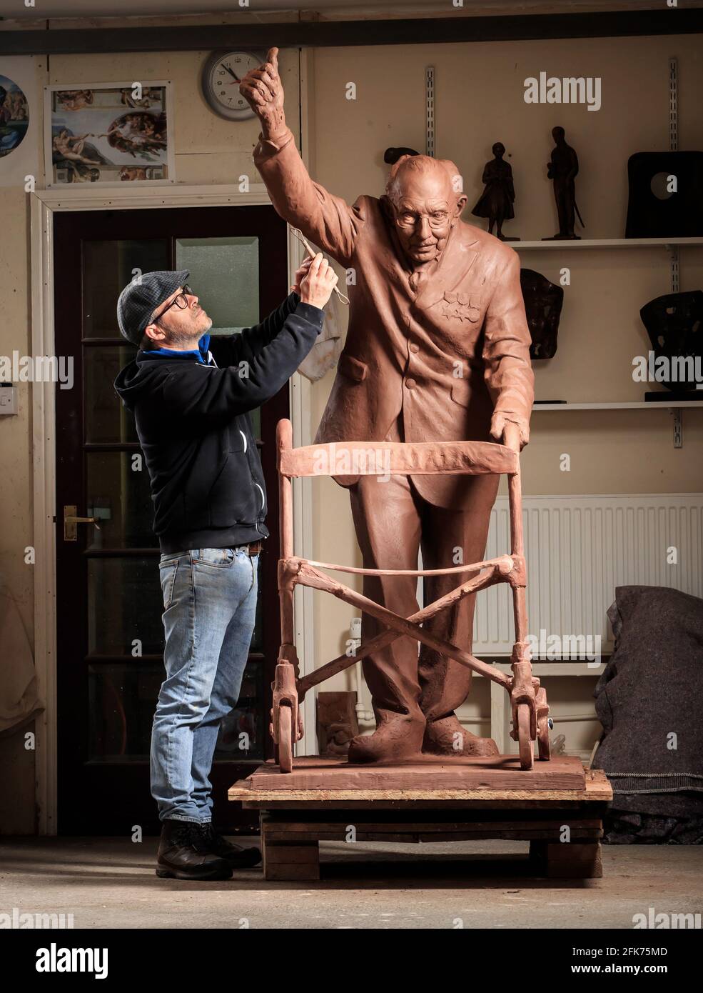 Andrian Melka puts the finishing touches to his two-metre high clay statue of Captain Sir Tom Moore at his home studio near York. The sculptor is crowdfunding to have the work cast in bronze so he can donate it to Leeds Teaching Hospitals NHS Trust. Picture date: Wednesday April 28, 2021. Stock Photo