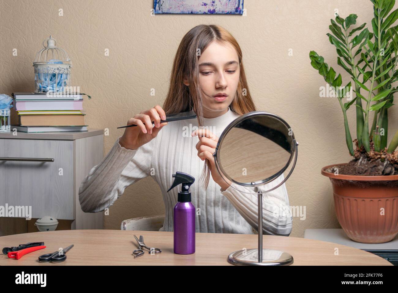teenage girl with a comb in her hand looks in the mirror. beautiful teenage girl doing her hair in front of the mirror in her room. Soft focus Stock Photo
