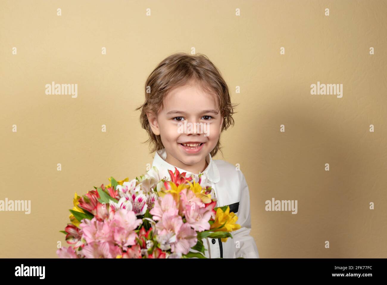 smiling handsome boy holds out a bouquet of colorful flowers. happy child gives a bouquet of multicolored alstroemeria. Soft focus Stock Photo