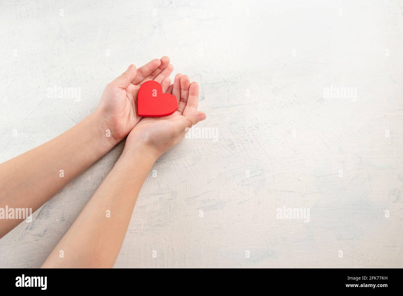 children hands holding red heart on white textured background. Concept ...
