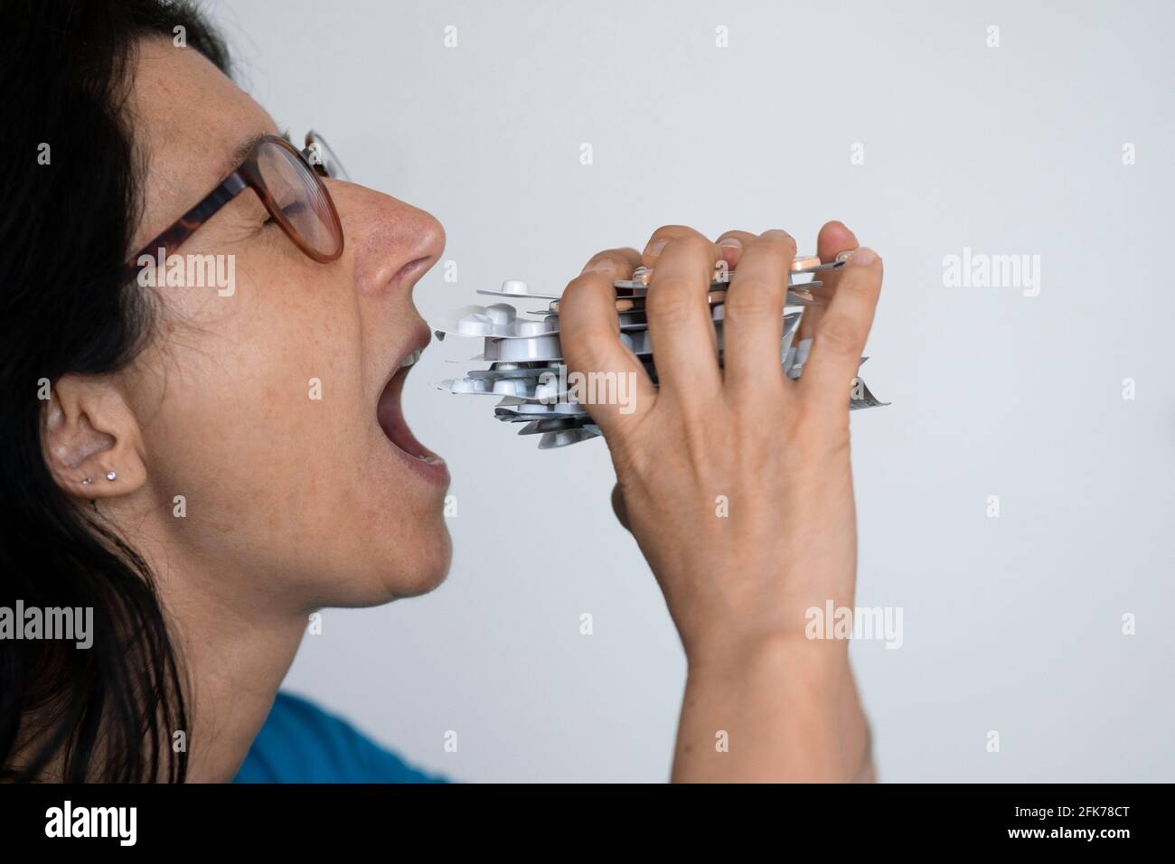 Middle-aged woman eats blister packs of pills like a sandwich. Drug addiction and abuse concept. Stock Photo