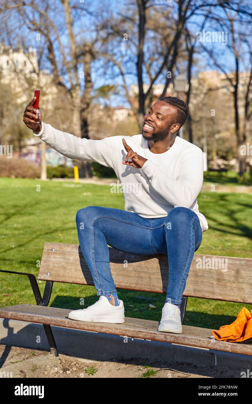 Young African American man sitting on a park bench, taking a self-portrait  with a smartphone. Happy black man. New normality. High quality photo Stock  Photo - Alamy