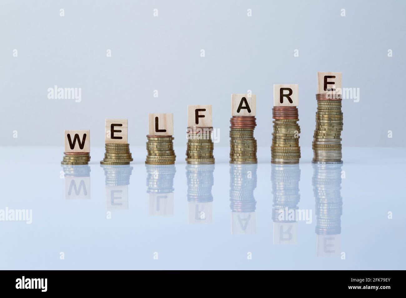 Word 'WELFARE' on wooden blocks on top of ascending stacks of coins on gray background. Concept photo of welfare, government support & social security Stock Photo