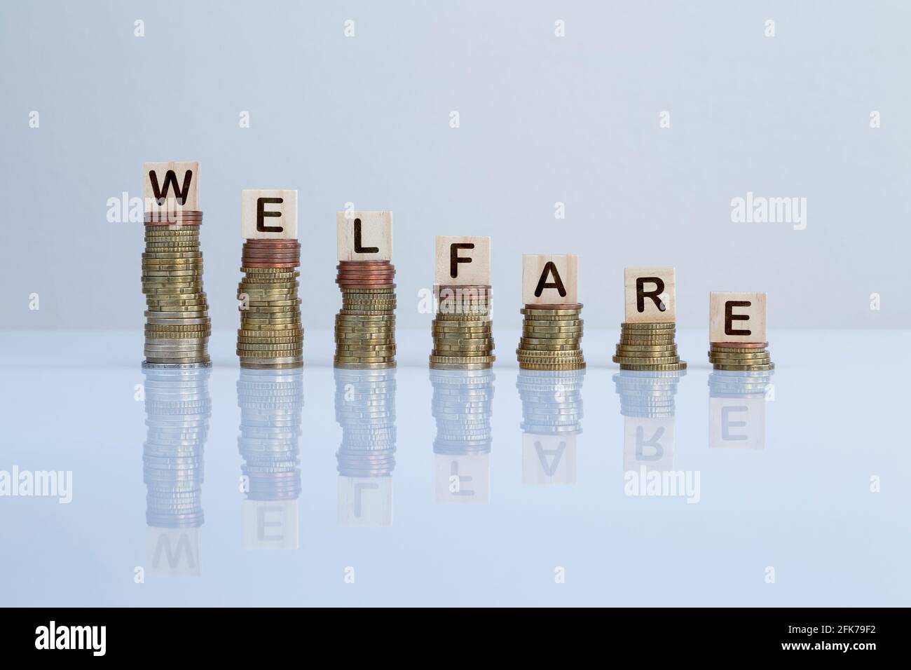 Word 'WELFARE' on wooden blocks on top of descending stacks of coins on gray. Concept photo of welfare, government support and social security. Stock Photo