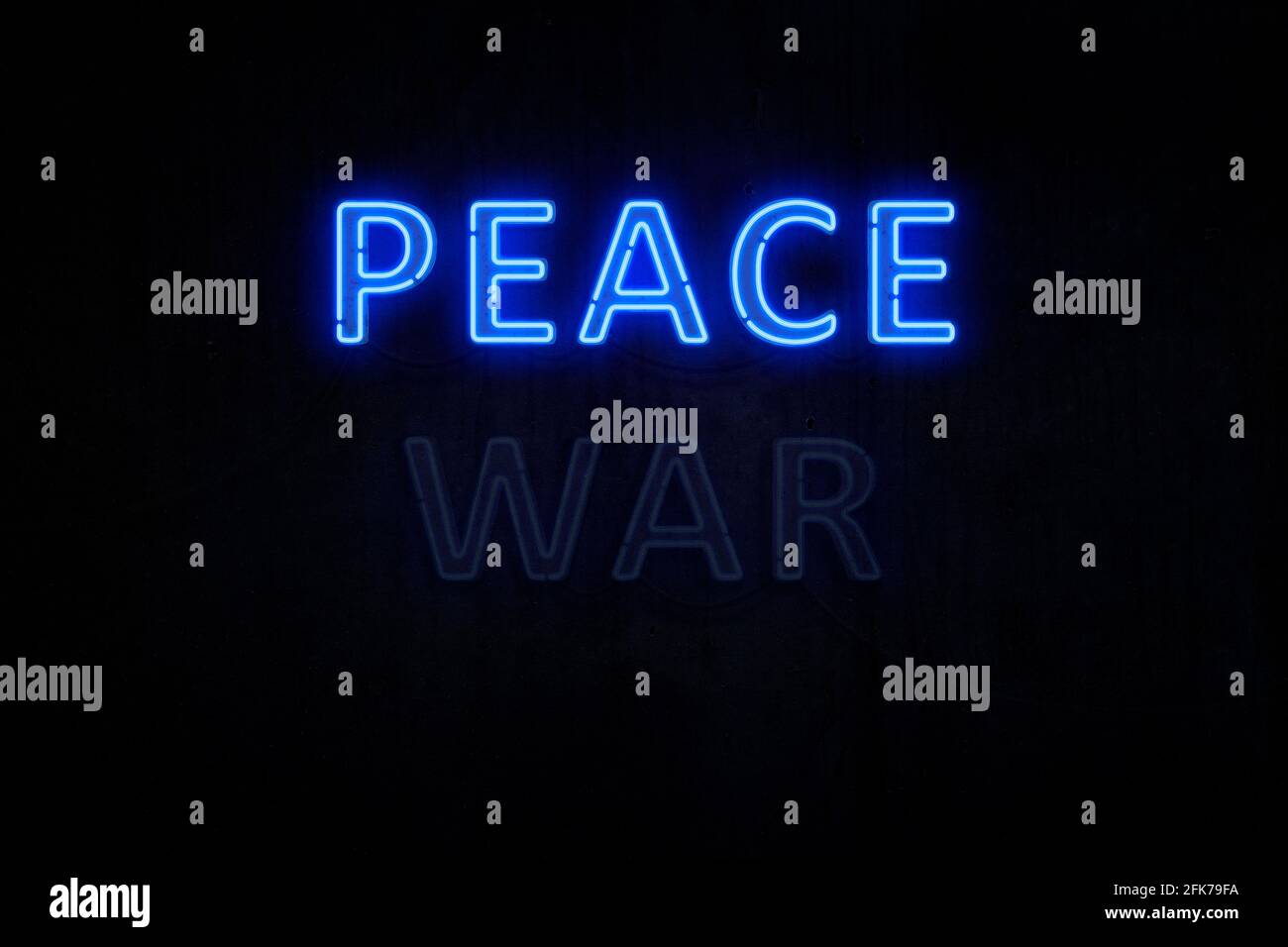 Illuminated and glowing blue 'PEACE' neon sign on dark, almost black, wall background. 'WAR' neon sign is off. Concept of how peace wins over war. Stock Photo