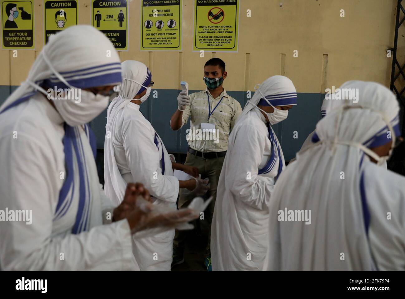 An election official checks the temperature of Catholic nuns from the Missionaries of Charity, the global order of nuns founded by Saint Mother Teresa, before they cast their vote outside a polling station during the eight and final phase of West Bengal state election, amid the spread of the coronavirus disease (COVID-19) in Kolkata, India, April 29, 2021. REUTERS/Rupak De Chowdhuri Stock Photo