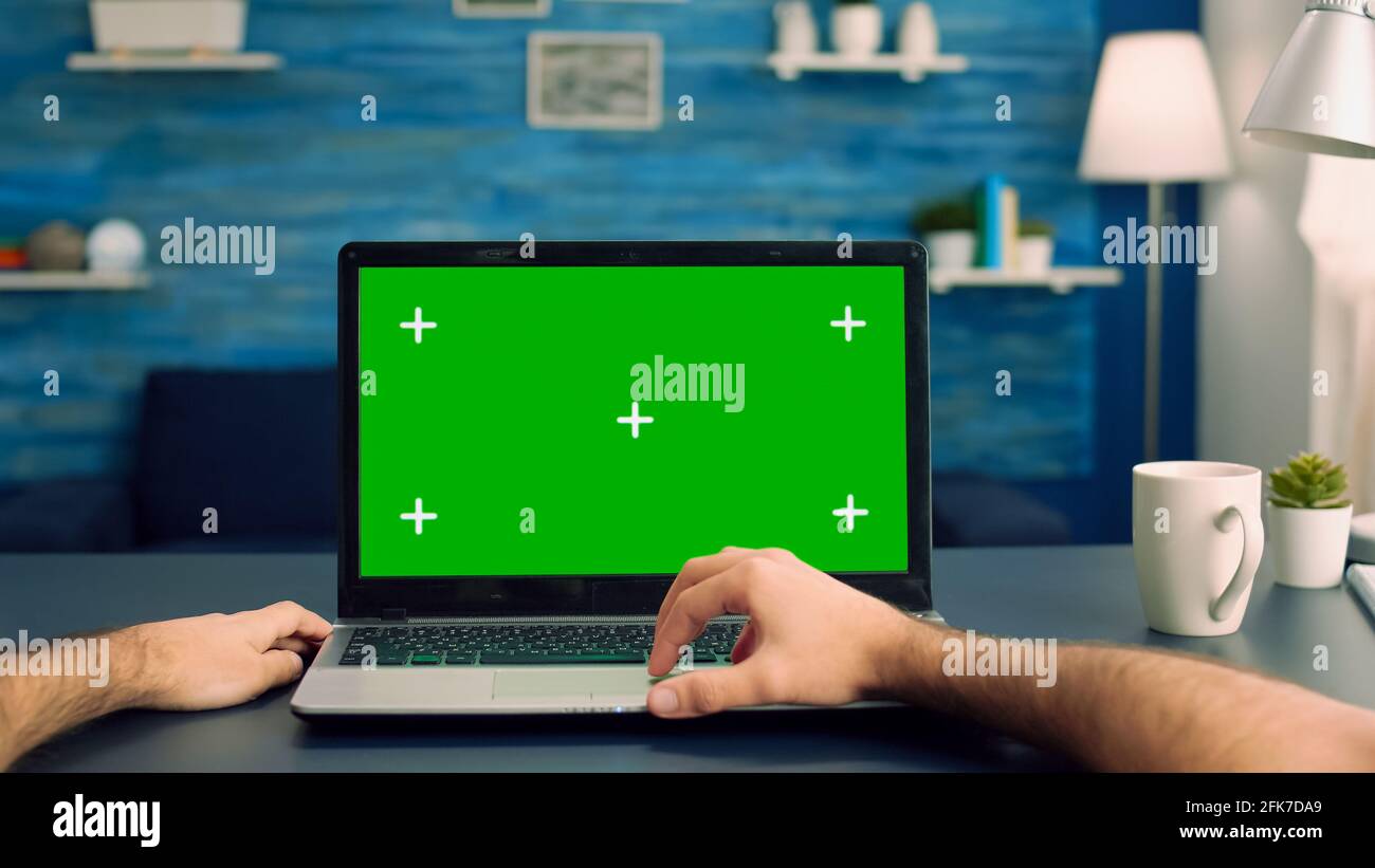 Point of view of man hands typing on laptop computer with mock up green  screen chroma key display for e commerce courses. Freelancer using isolated  device standing on desk table in home