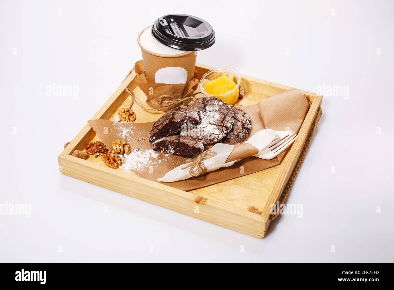 Chocolate cookies lie on kraft paper and coffee on a wooden rustic tray on a white background. Paper cup and disposable tableware made of eco-friendly Stock Photo