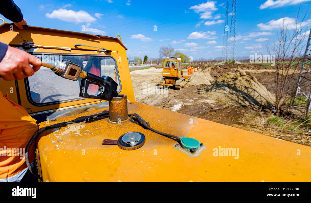 Worker holding fuel pump gun inserted in the reservoir of construction
