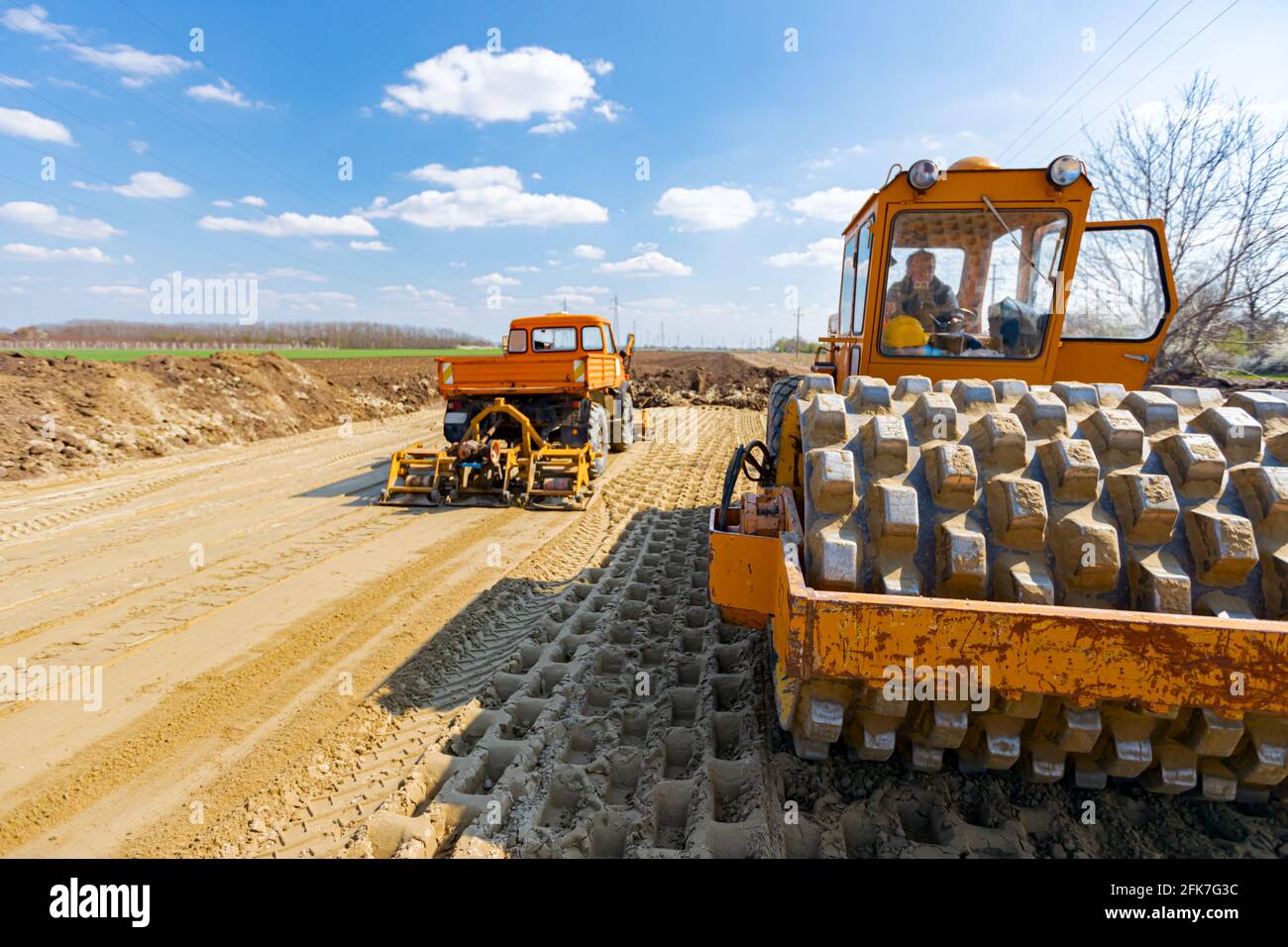 Road roller with spikes and truck with mounted plate vibration compactor  are compacting, leveling sand for road foundation at building site Stock  Photo - Alamy