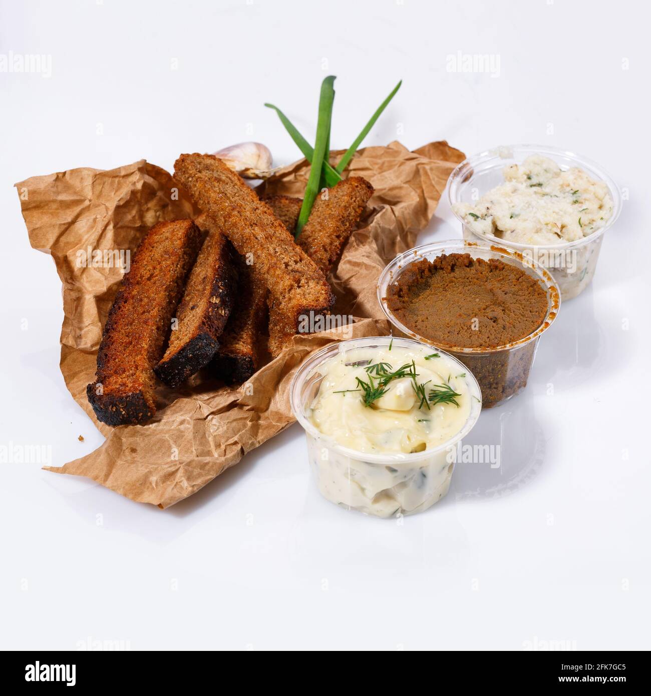 Crackers of black bread lie on kraft paper, mayonnaise and garlic sauce, meat pate, lard with dill on a white background. Side view. Stock Photo