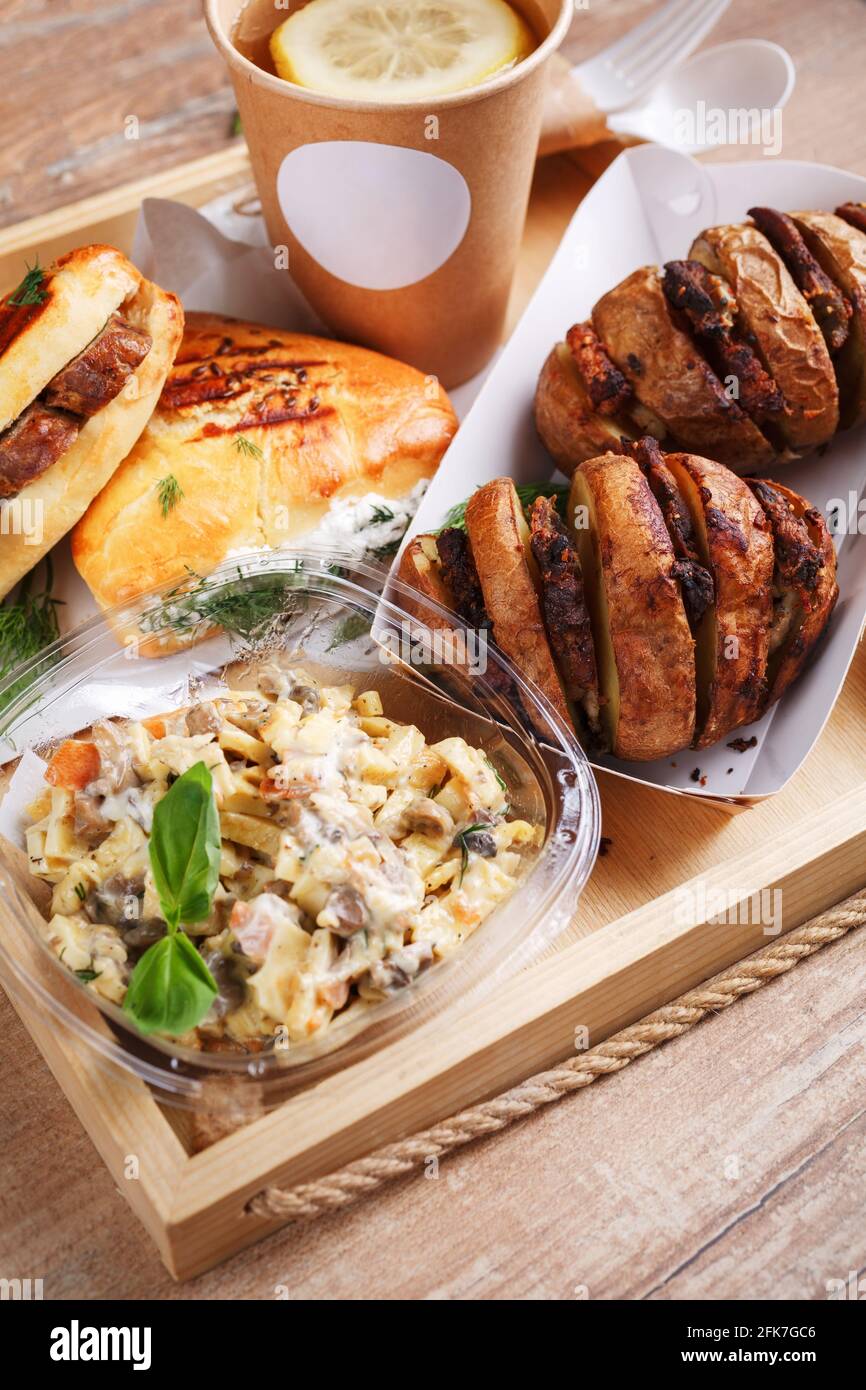 Disposable tableware, lemon tea, slate, mouth-watering sausage rolls and dill and baked potatoes with meat on a wooden tray. Place for text. Street fo Stock Photo
