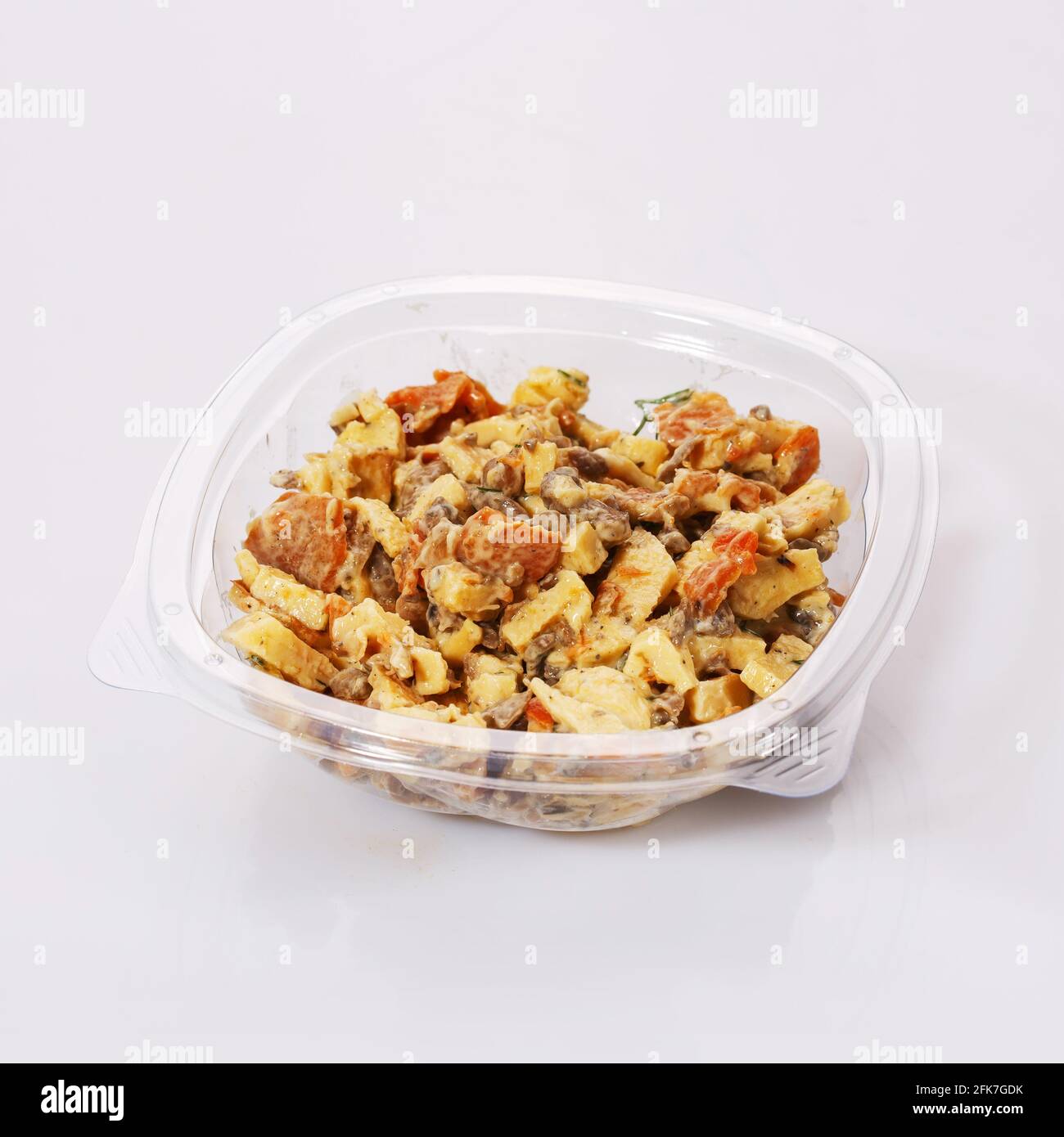 Salad of carrots, meat, cheese and sauce in a transparent plastic bowl on a white background. Tasty dish. Stock Photo