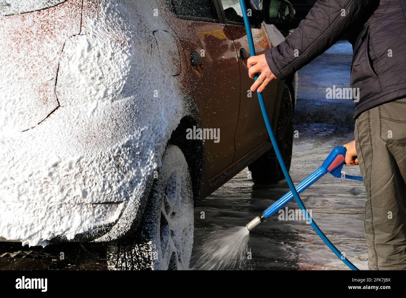 Man washes his orange car at car wash. Cleaning with soap suds at self