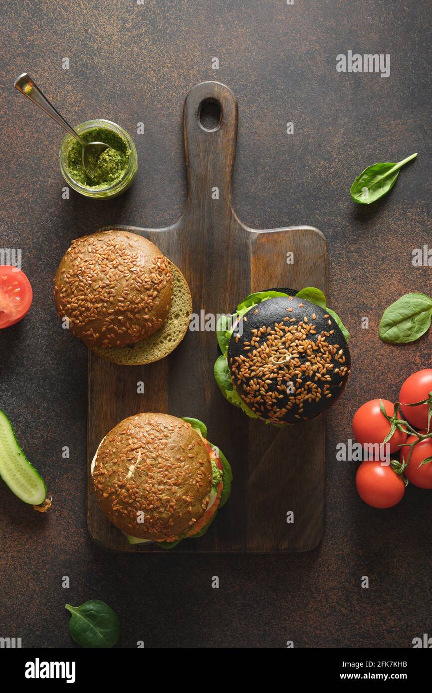 Trendy vegan burgers with vegetable meatballs, tomatoes, cucumber, sauce pesto as plant based meat on a brown background. View from above. Vertical fo Stock Photo