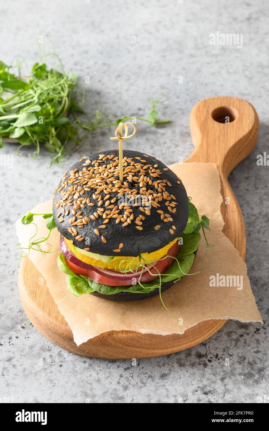 Vegan burger of black buns, vegetable meatballs, spinach, tomatoes, salad, peas microgreens on grey stone table. Close up. Horizontal orientation. Stock Photo