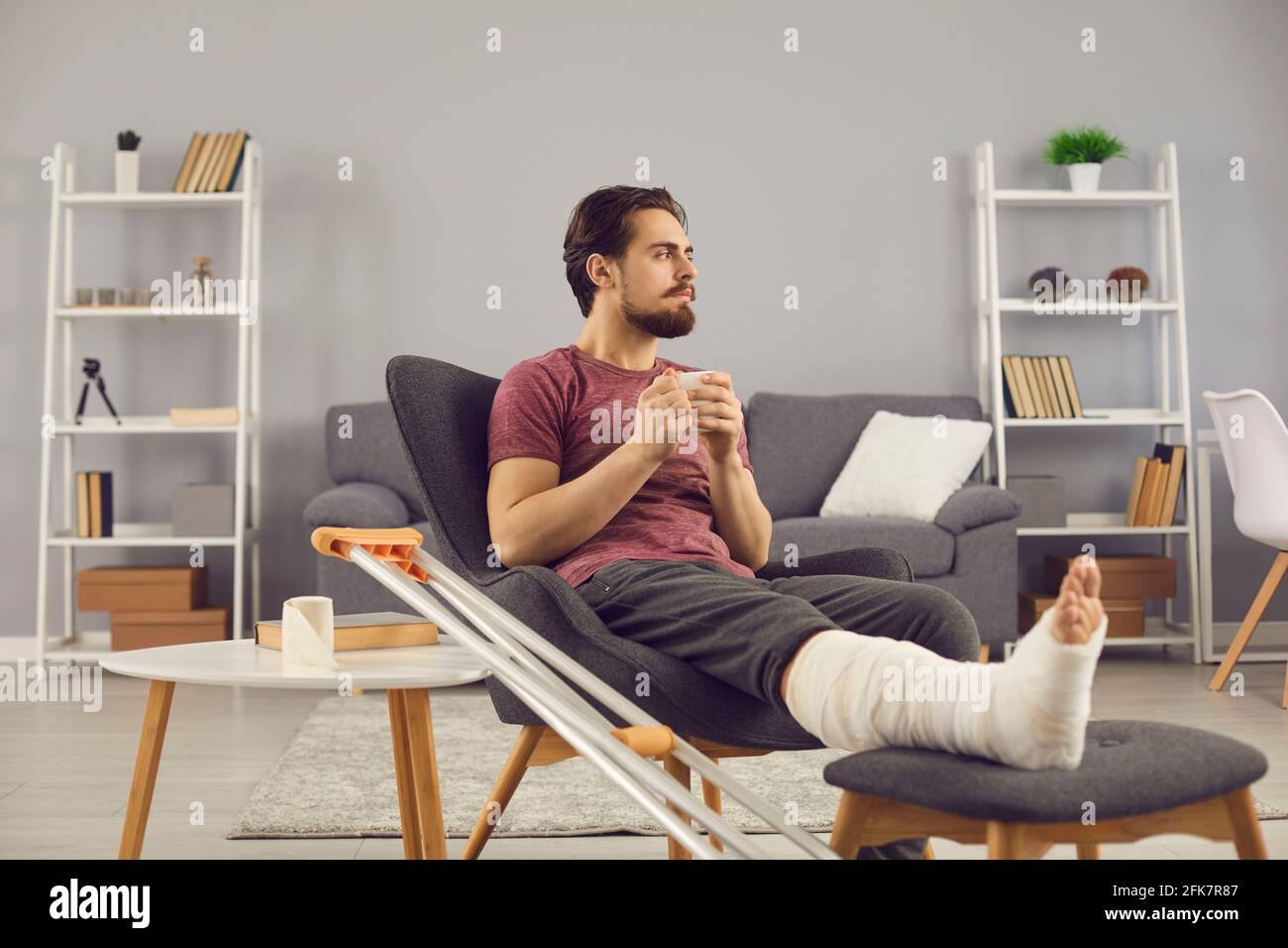 Man with broken leg sitting in armchair, thinking about his injury and