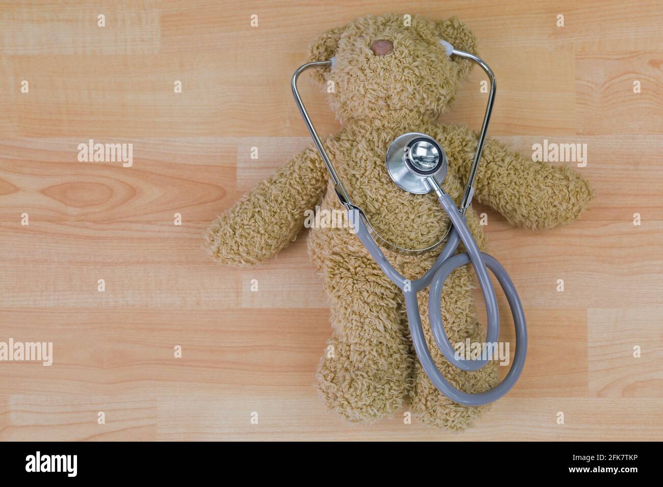 Teddy bear on wooden floor with stethoscope, acoustic medical device with earpieces in ears Stock Photo