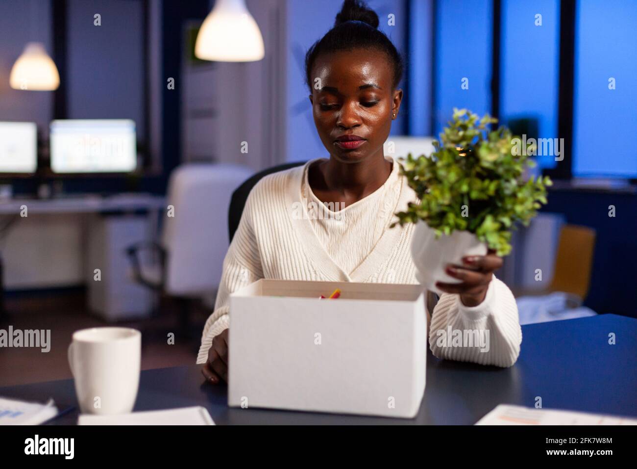 Depressed african woman after being dismissed from work late at night. Unemployed packing things late at night. woman leaving workplace office in midnight. Stock Photo