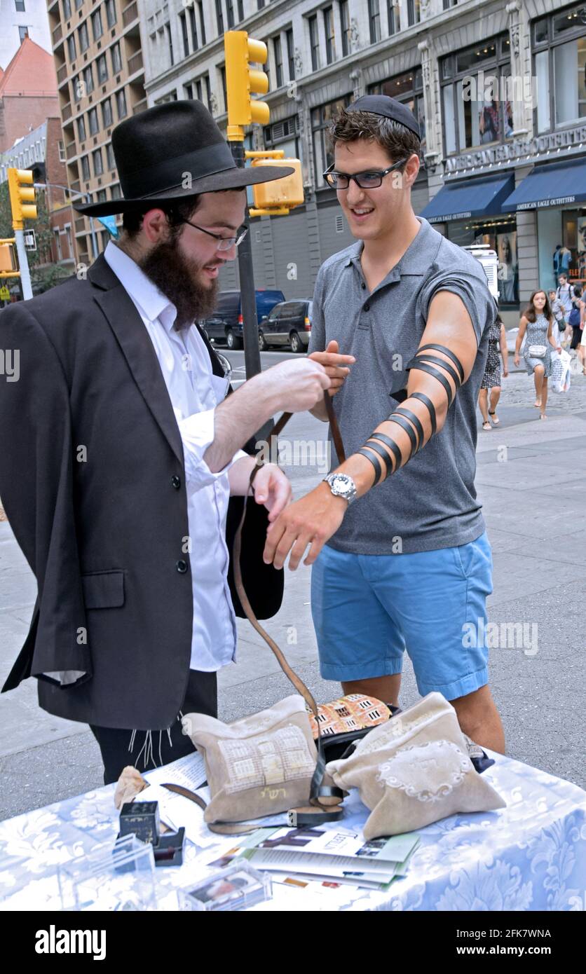 As part of the Chabad Lubavitch outreach, a young Jewish student helps another Jew do the good deed of wearing phylacteries. In Union Square Park, NYC. Stock Photo