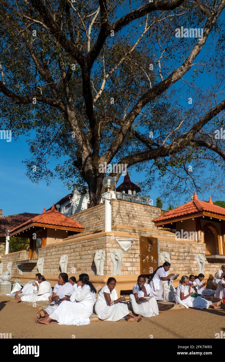Kandy, Sri Lanka: some women dressed in white sit eating inside the temple of sacred tooth relic Stock Photo