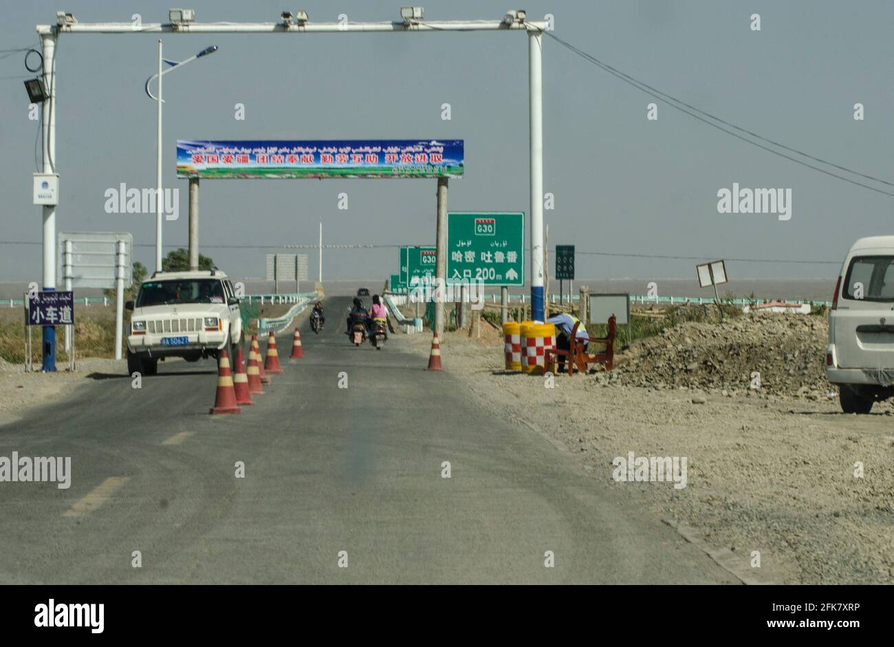 A policeman looks at his phone at a barriers on a road security checkpoint with cameras and face recognition to control the movement of Uighur (Uyghur) people on the outskirts of Kashgar in the South of  Xinjiang, China, PRC. © Time-Snaps Stock Photo