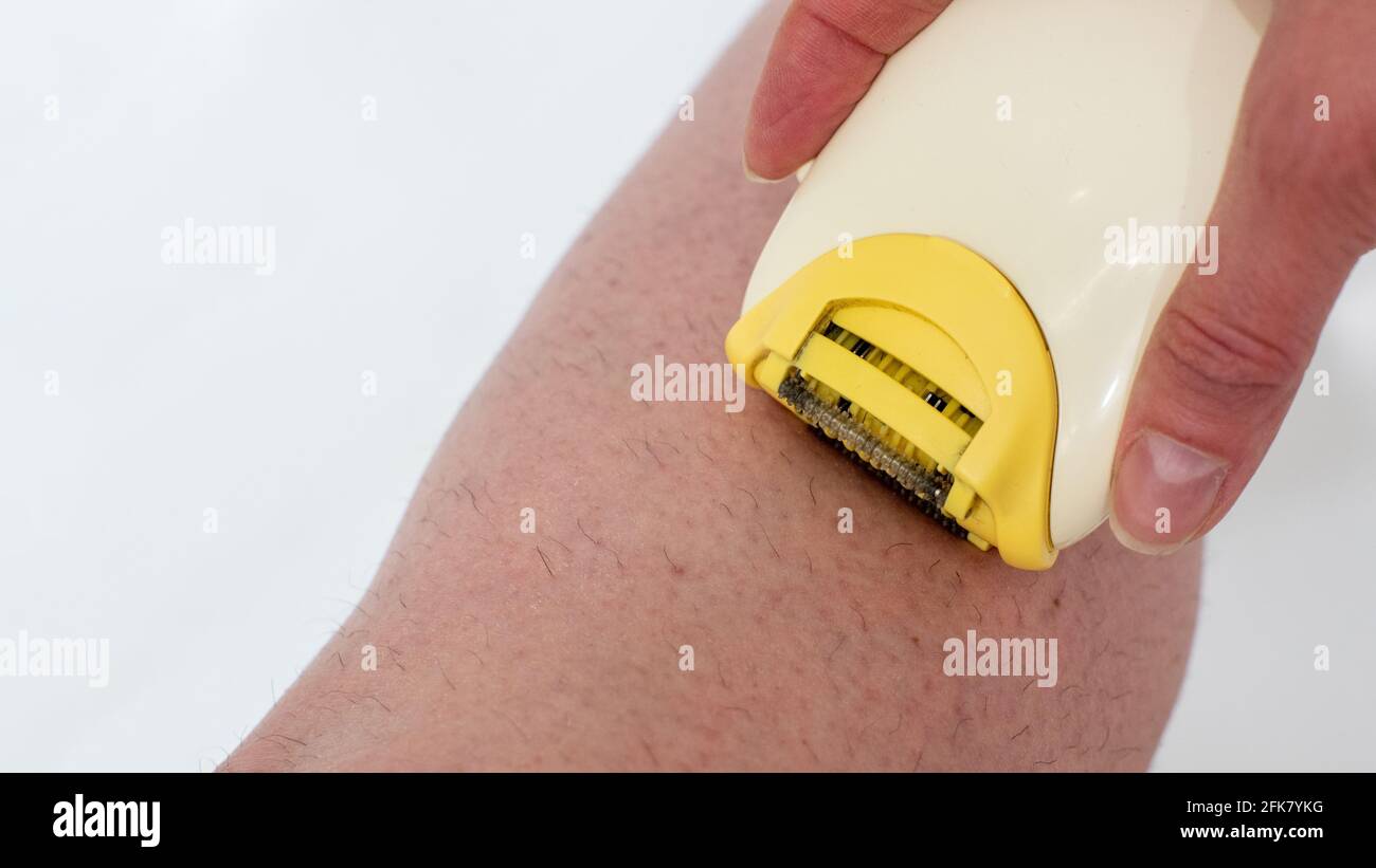 Close-up of a female hand removes excess hairs from the legs with an electric razor. Home beauty treatments. Skin hygiene body care concept. Depilatio Stock Photo