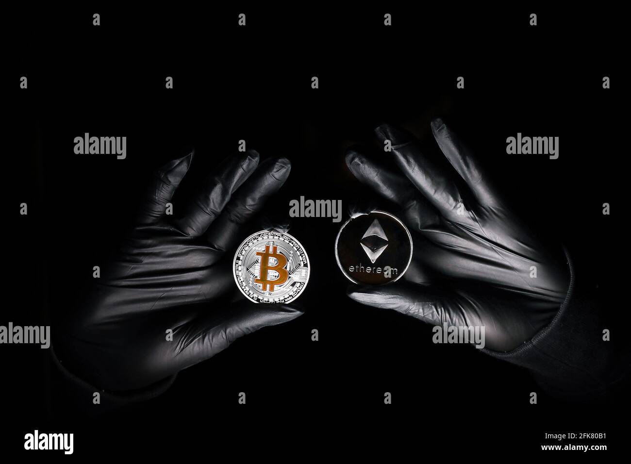 Hands in a black gloves holding bitcoin and Ethereum coin against black background. International hacker is trying to steel your crypto currencys. Blockchain security. Stock Photo
