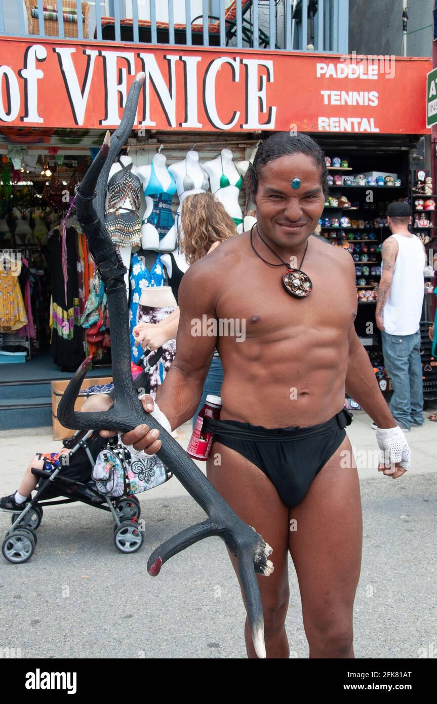 A dark-skinned man with black hair, wearing a bathing suit, and holding an antler from an antelope, a busker, on the Venice Beach Boardwalk in Calif. Stock Photo