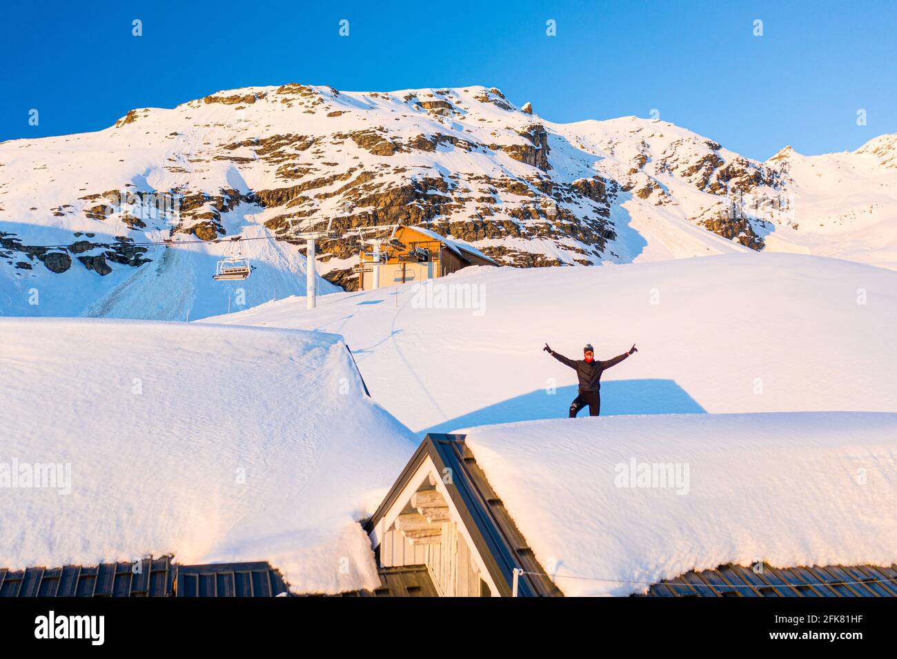 Man posing on the roof of a snow covered cottage like residence in Val Thorens, A  small ski town located at the base of french alps mountain range. Stock Photo