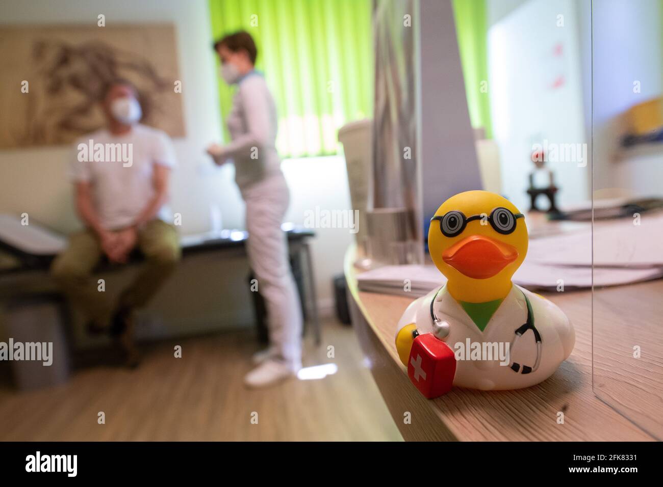 Saulheim, Germany. 29th Apr, 2021. A rubber ducky with a doctor's coat is standing out of the table in the family practice of Barbara Römer, specialist for general medicine and state chairwoman of the Hausärzteverband Rheinland-Pfalz e.V. (Rhineland-Palatinate association of family doctors). Römer is talking in the background to a patient who has been vaccinated against the coronavirus. Credit: Sebastian Gollnow/dpa/Alamy Live News Stock Photo