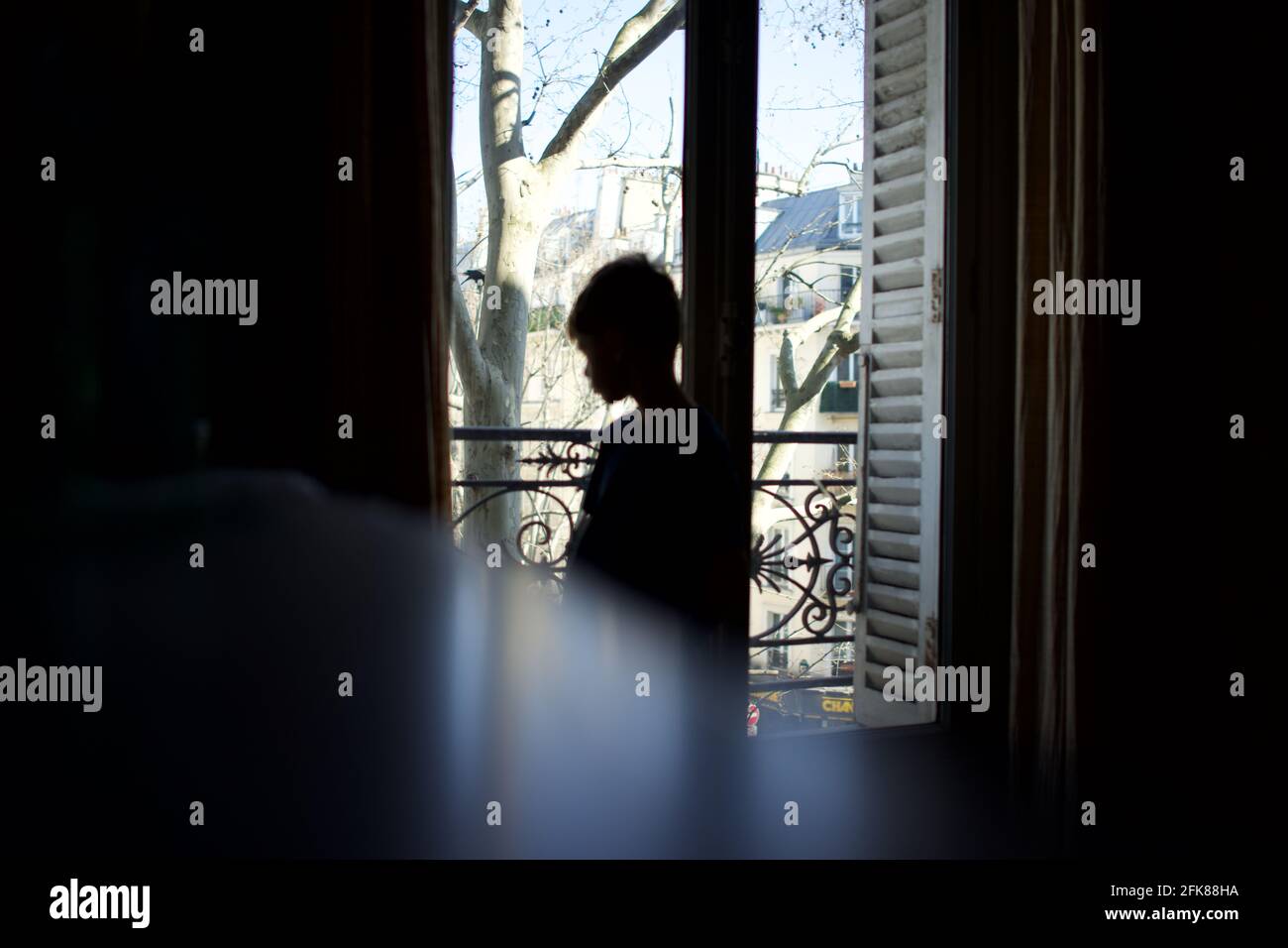Child standing, silhouetted, looking out of window, in profile, vulnerable, alone - April 2021 confinement, Paris, France Stock Photo
