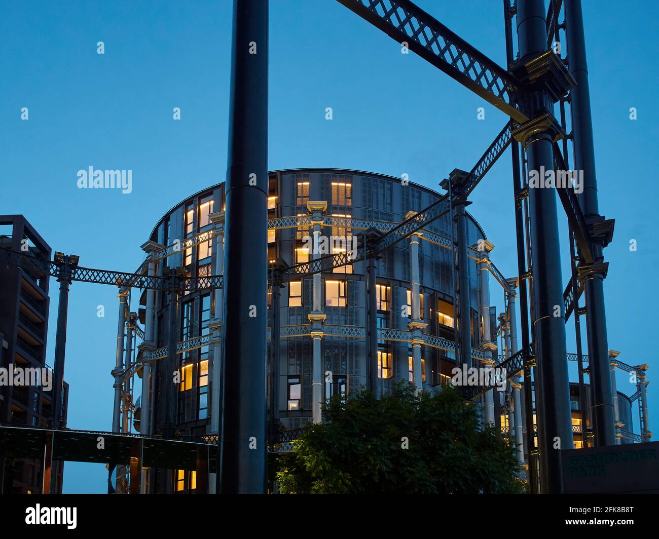 A group of gasometers, now flats following redevelopment as part of an urban renewal project. Warm light comes from the windows behind the ironwork. Stock Photo