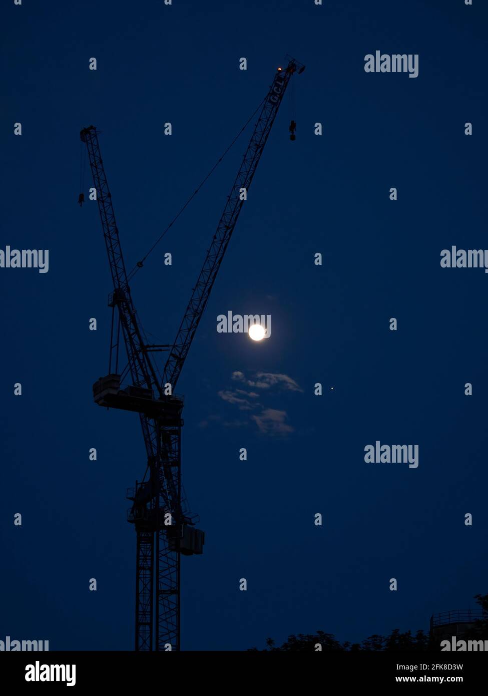 Two immense tower cranes in silhouette against a deep blue twilight sky ...