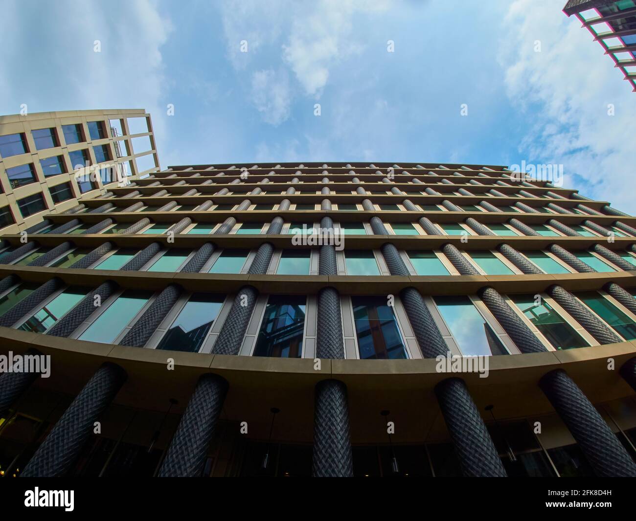 A newly built office building, part of a more general urban renewal project, seen looking up its facade to a bright blue, cloud speckled summer sky. Stock Photo