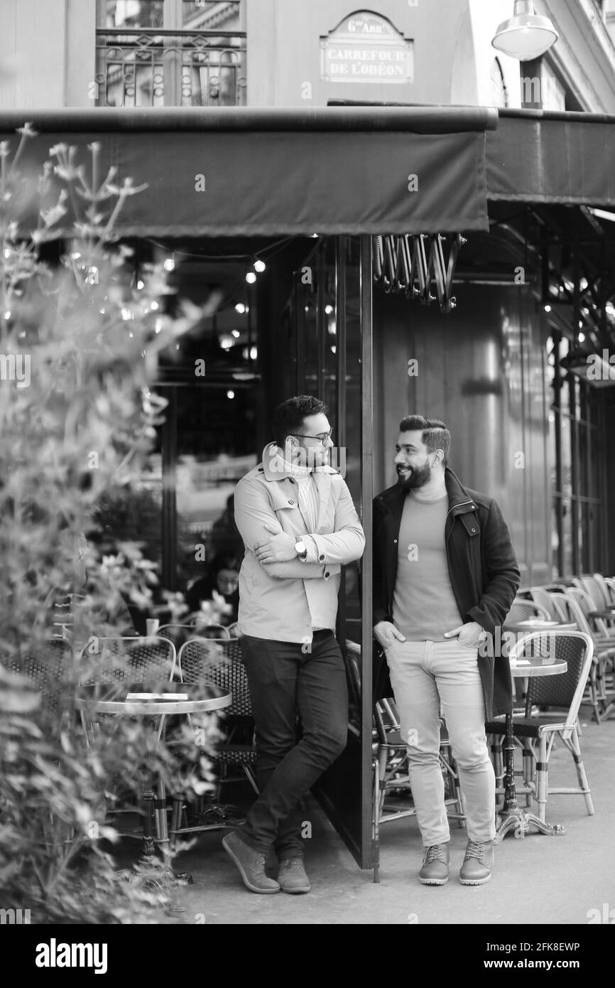 Black and white photo of male friends standing and talking at street cafe. Stock Photo