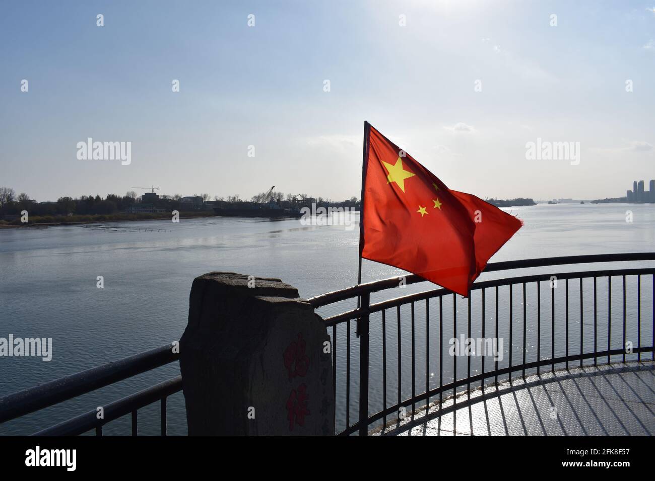 Chinese flag waving above river at China/North Korea border [Yalu River Broken Bridge, Dandong, China, Dec. 1st 2016] Stock Photo
