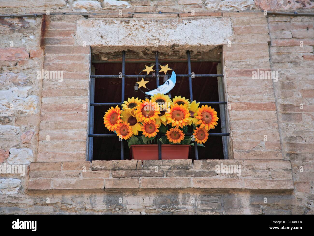 Fenster mit einem Strauss Plastikblumen, Sonnenblumen, in der Altstadt von Assisi, Umbrien, Italien Stock Photo
