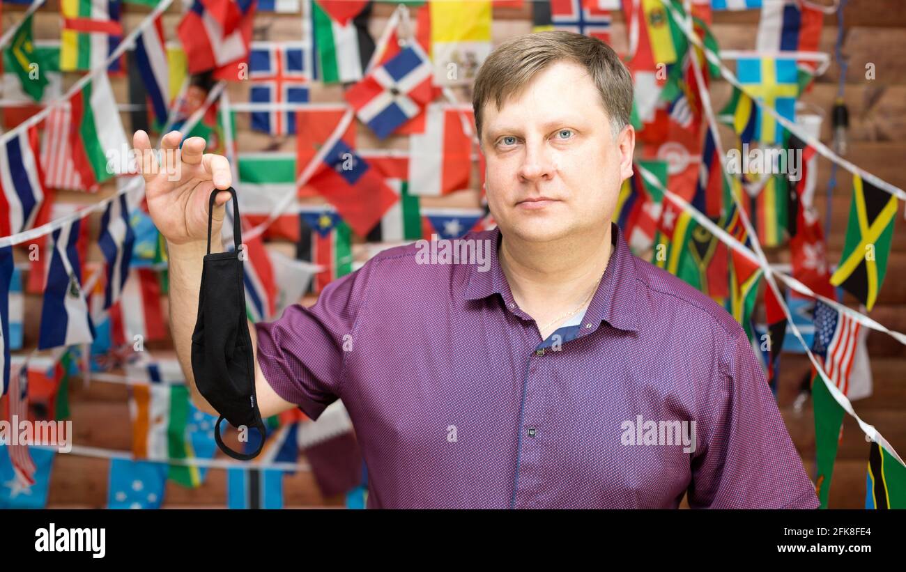 A man shares a used medical mask in his hands against the background of country flags. Stock Photo