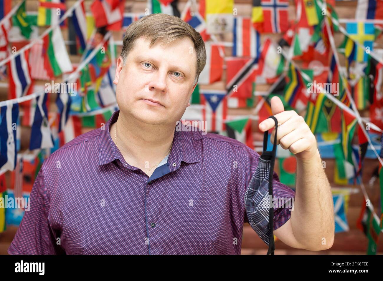 A man shares a used medical mask in his hands against background of country flags. Stock Photo
