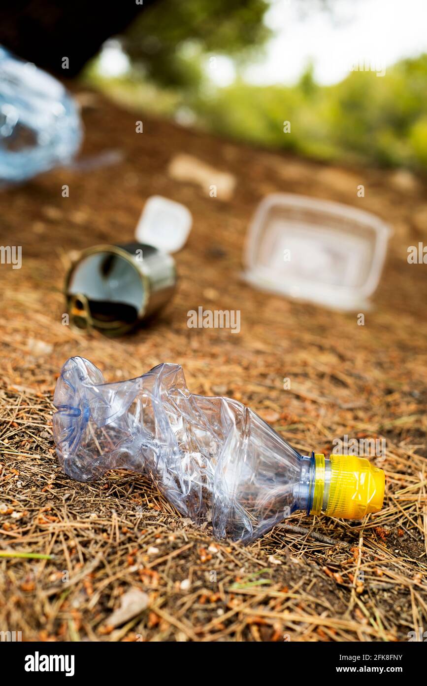 closeup of a used plastic bottle and some other garbage, such as used food cans and plastic containers, thrown on the ground of a forest Stock Photo
