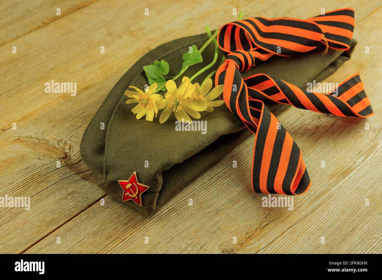 Military cap, yellow flowers, George ribbon on wooden background. 9 May Victory Day holiday card. Stock Photo