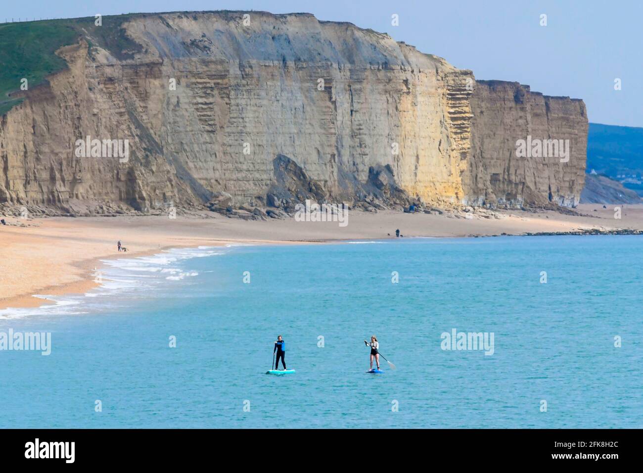 West Bay, Dorset, UK.  29th April 2021.  UK Weather.  Two paddle boarders on the sea off the beach at the seaside resort of West Bay in Dorset on day of cloud and warm sunny spells.  Picture Credit: Graham Hunt/Alamy Live News Stock Photo