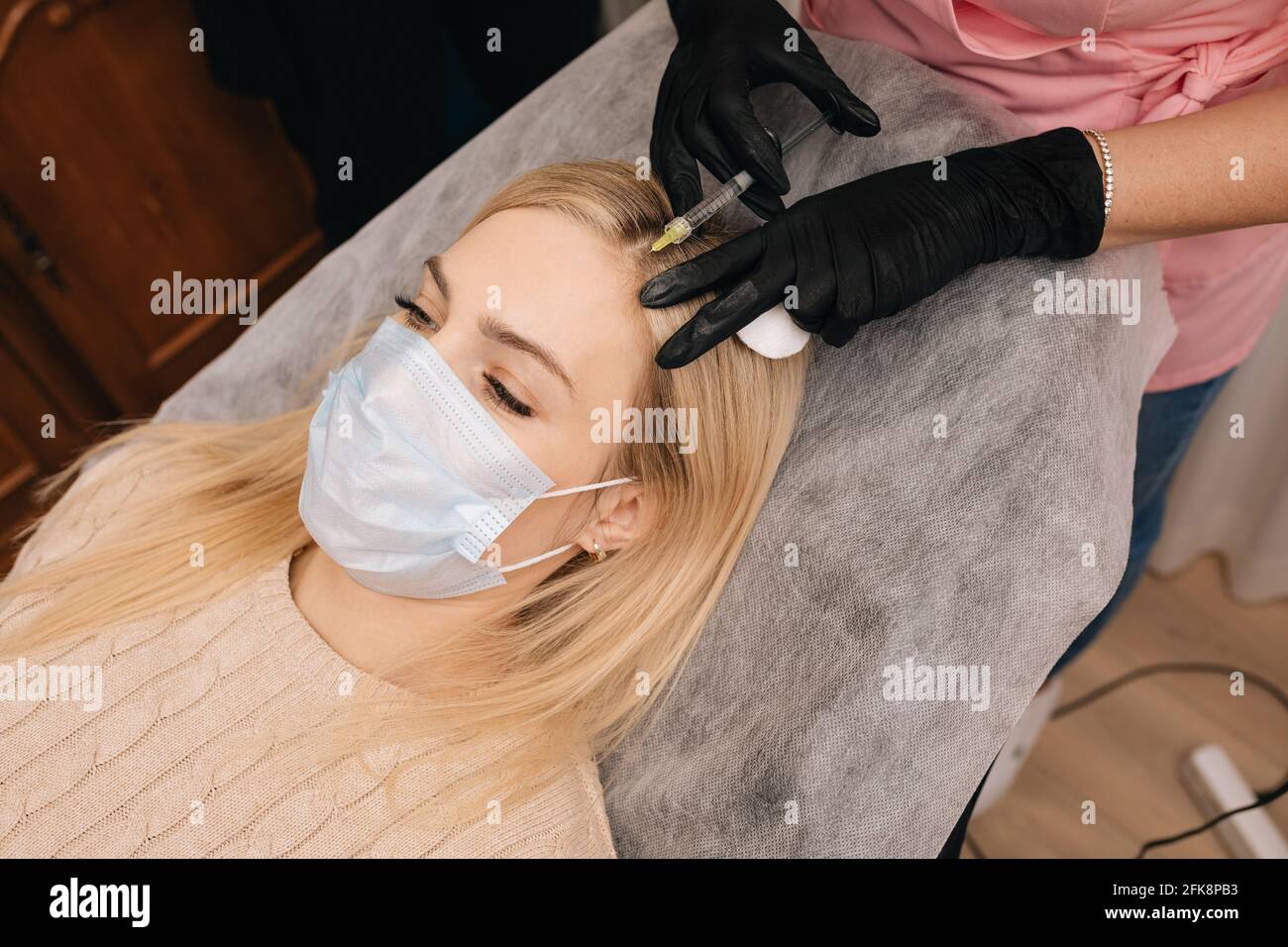 Beautician gloves gives injection into the head of blonde woman. Mesotherapy, hair loss therapy. Hair restoration concept. Stock Photo
