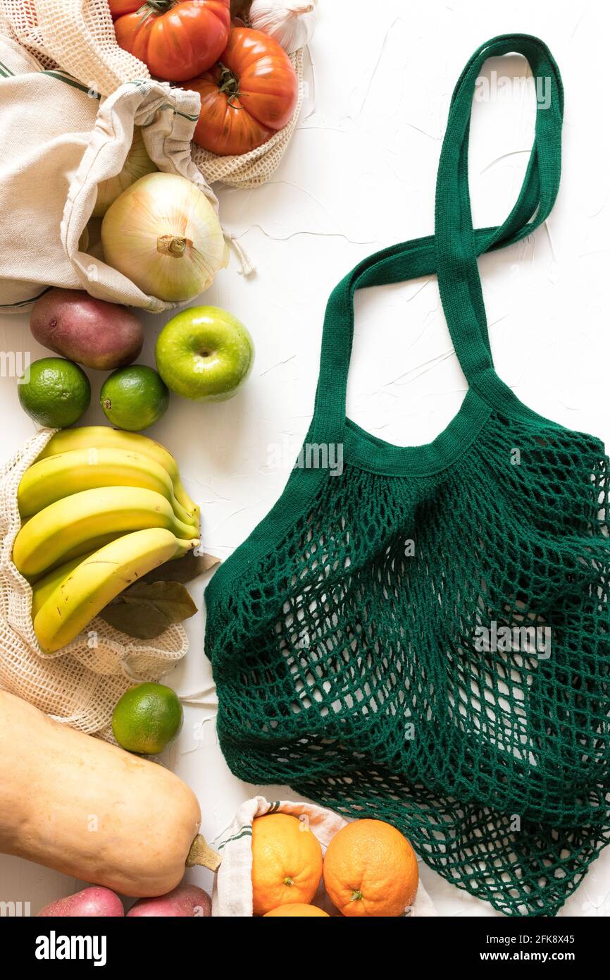 Raw healthy colorful vegetables and fruit with a green mesh bag in the right part of the scene on a white background. Stock Photo