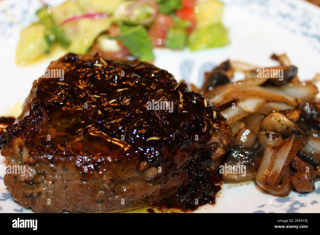 Close-up of a fried steak with a red wine reduction, mushrooms and onions, and a salad. Stock Photo