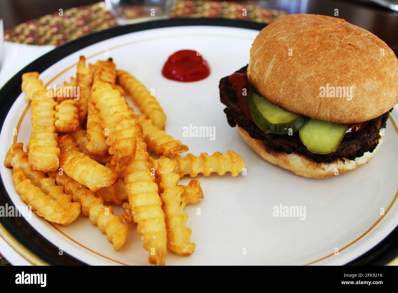 Close-up of a hamburger and French fries on a plate, with a dollop of ketchup. Stock Photo