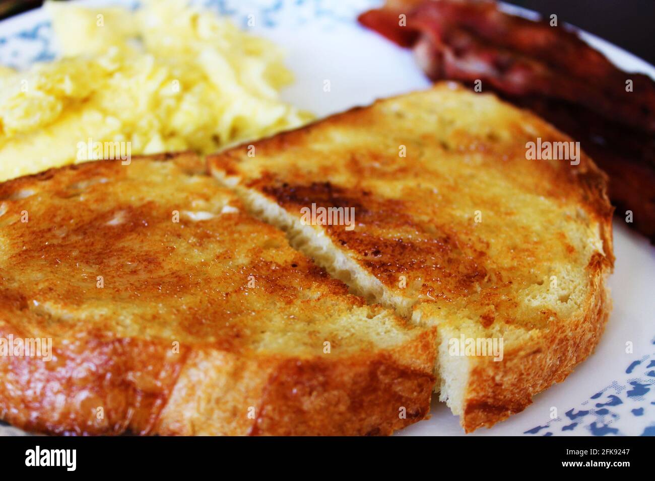 Close-up of a slice of toast on a plate, bacon and scrambled eggs out of focus in the background. Stock Photo